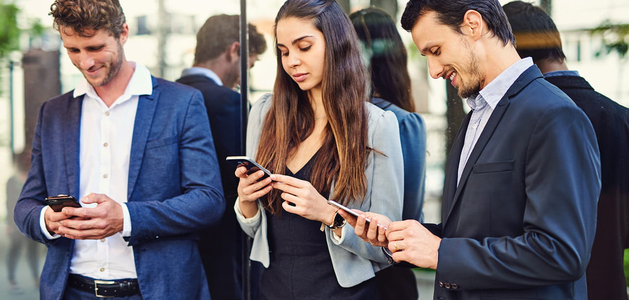 Business professionals using smartphones outside a modern office building, representing mobile-first digital engagement and connected business communication.